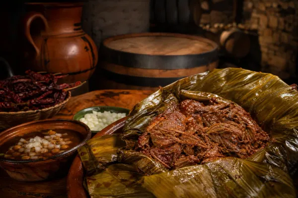Barbacoa de borrego envuelta en pencas de maguey con adobo añejado en barril de roble servida con consomé