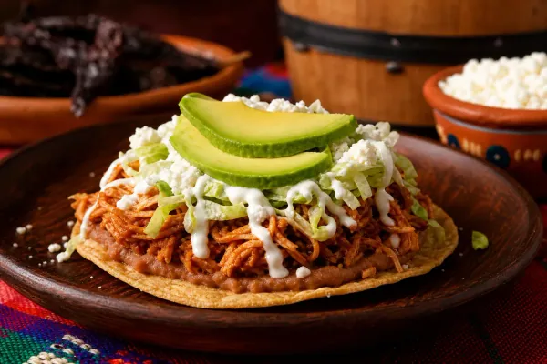 Tinga de pollo con salsa adobada añejada en barril servida sobre tostadas con frijoles y crema